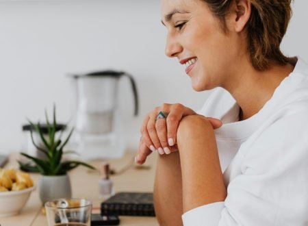 Woman in white top smiling while using a laptop at a bright home desk. Relaxed work atmosphere.