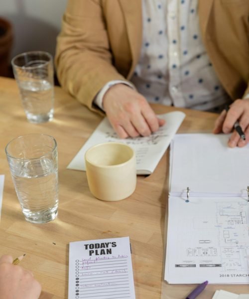 A collaborative office meeting with notebooks, coffee, and planning notes on a wooden table.